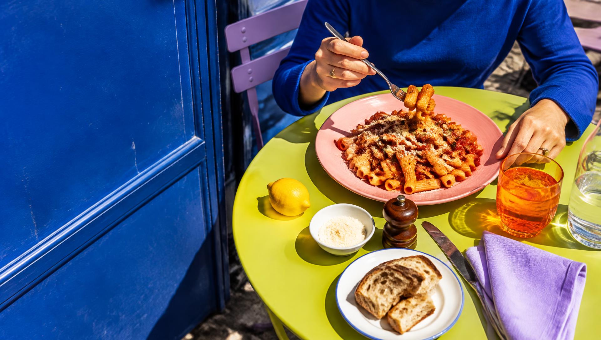 Mise en scène éditoriale : table matcha, assiette rose et pâtes sur une terrasse bleu vif